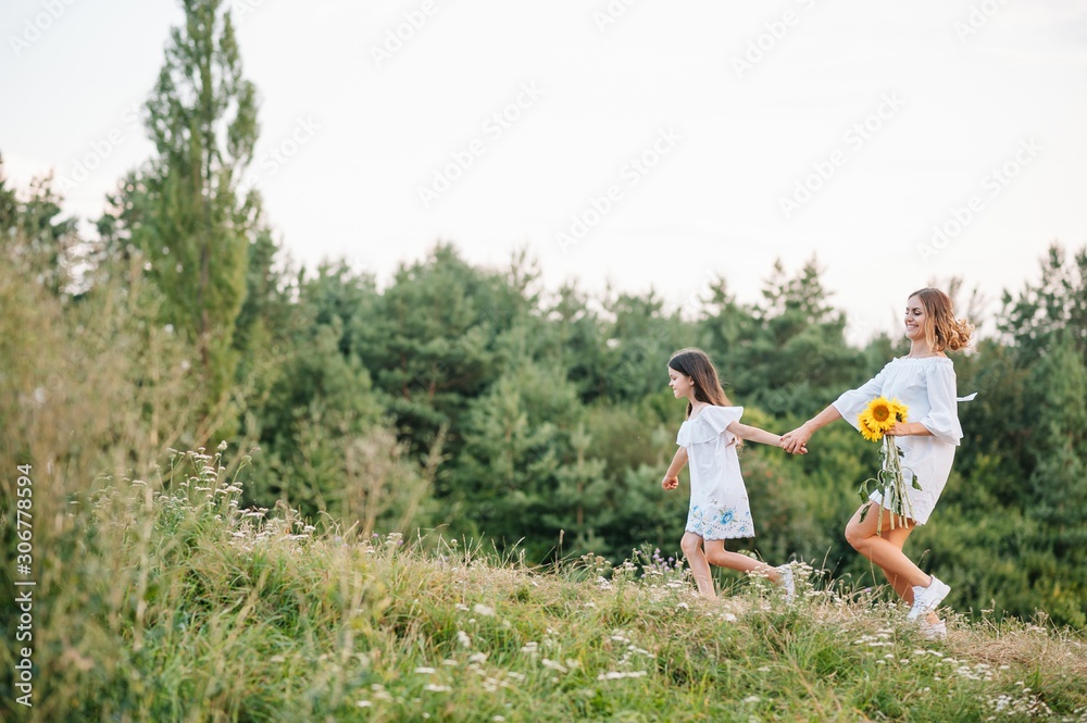 Cheerful mother and her little daughter having fun together in the summer background. Happy family in the nature background. Cute girls with colorful flowers. Cheerful mother and her little daughter having fun together in the summer background. Happy family in the nature background. Cute girls with colorful flowers.