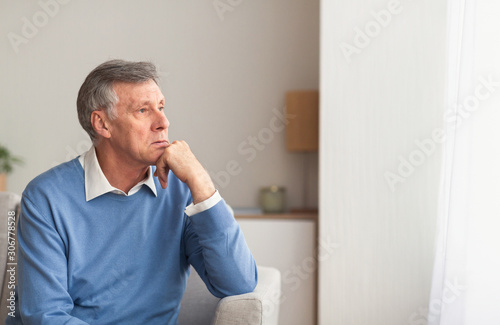 Upset Senior Gentleman Sitting On Sofa At Home After Retirement
