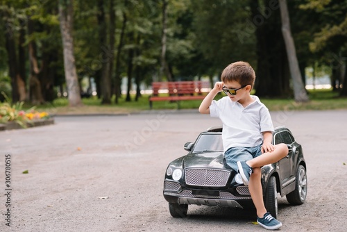 Cute boy in riding a black electric car in the park. Funny boy rides on a toy electric car. Copy space. photo