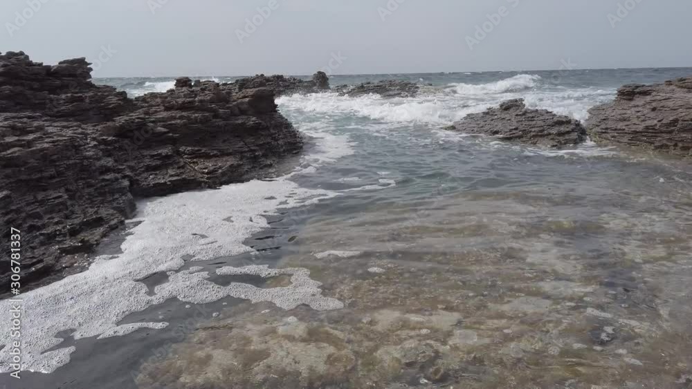 Low angle pan shot rocky bay with emerald sea water crashing on the rocks with foam , Sardinia region, Italy Low angle pan shot rocky bay with emerald sea water crashing on the rocks with foam , Sardinia region, Italy