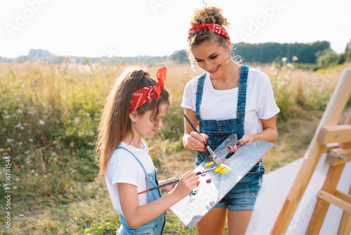 Beautiful mother with daughter. Family in a summer park. Little girl drawing