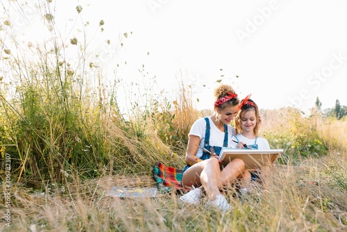mother teaches daughter paint in park. Sunny nature, mom and daughter paint a picture in a park , painting a Little Child, Child Creativity. Mother's Day