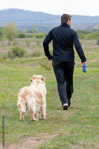 Young man running with your golden retriever dog on the meadow
