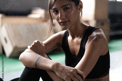 Young woman sitting on floor after her workout and looking down. Female athlete taking rest after fitness training