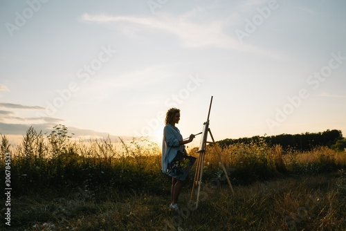 Pretty woman is painting. Open air session. Cute woman draws a picture at sunset. girl artist