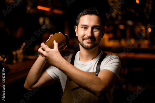 Professional male bartender holding a steel brown shaker making a cocktail