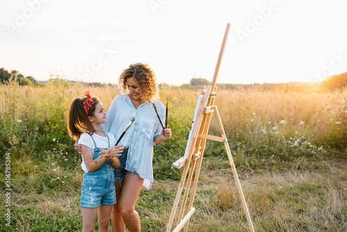 mother teaches daughter paint in park. Sunny nature, mom and daughter paint a picture in a park , painting a Little Child, Child Creativity. Mother's Day