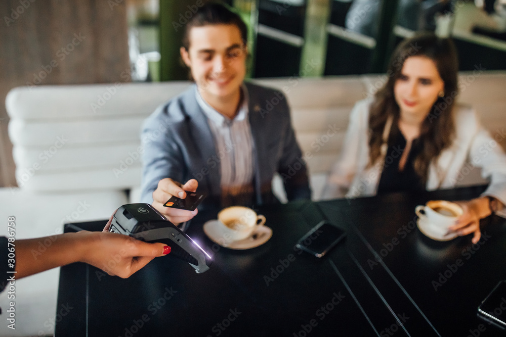 Partial view of couple sitting at table in restaurant while man paying for dinner by credit card and phone for waitress.
