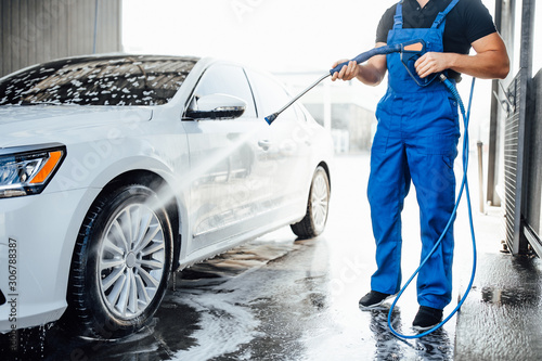 Professional washer in blue uniform washing luxury car with water gun on an open air car wash. Close up photo. photo
