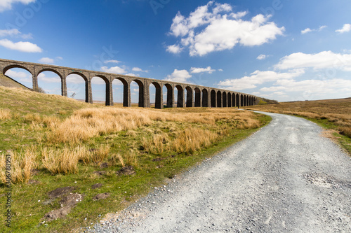 Path leading to arches of a railway viaduct, blue sky and clouds wide angle photo