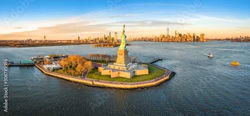Aerial panorama of the Statue of Liberty in front of Jersey City and New York City skylines at sunset.