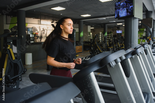 Woman trains on a treadmill in the gym. Young fitness girl running on treadmill machine. Sports exercises for weight loss.