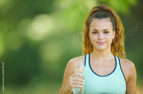 Beautiful young brunette woman (Caucasian) working out in park - holding water bottle