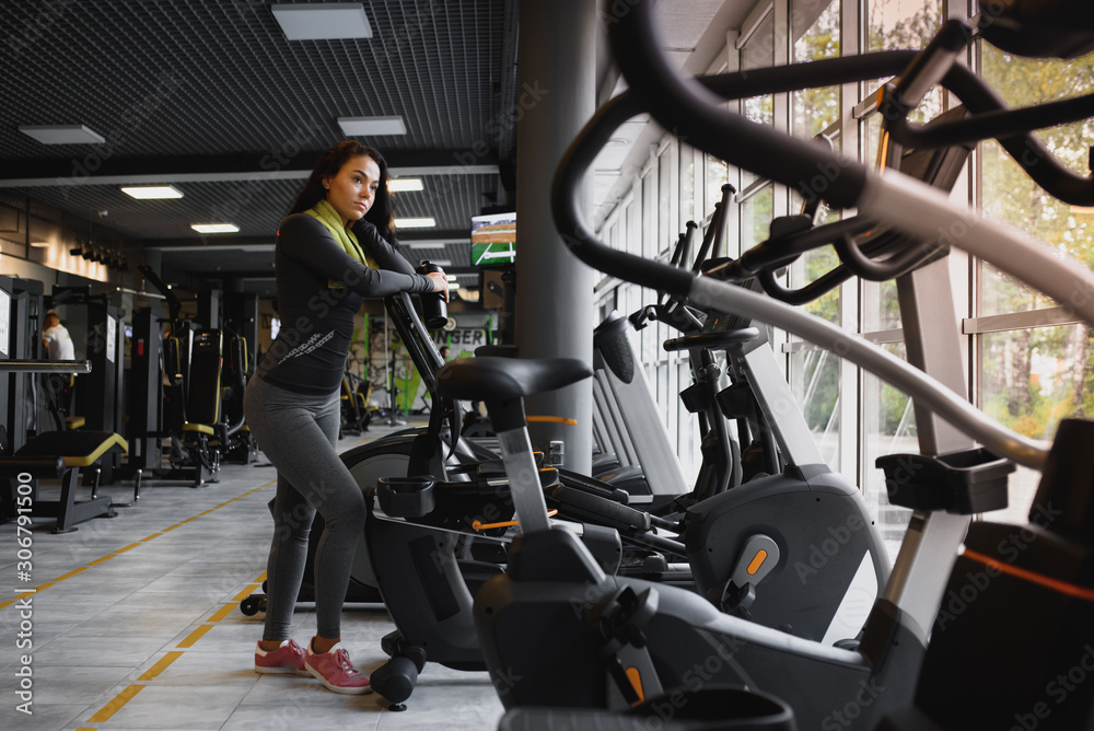 Fototapeta premium Young woman drinking water and taking a break after workout in gym,