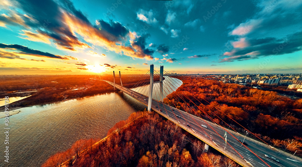 Beautiful panoramic aerial drone view to cable-stayed Siekierkowski Bridge over the Vistula river and Warsaw City skyscrapers, Poland in gold red autumn colors in November evening at sunset