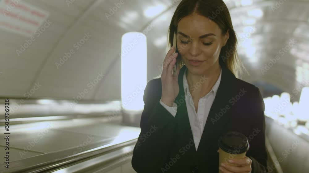 Close up shot of young female entrepreneur speaking on mobile phone with her colleague and drinking coffee from paper cup Close up shot of young female entrepreneur speaking on mobile phone with her colleague and drinking coffee from paper cup