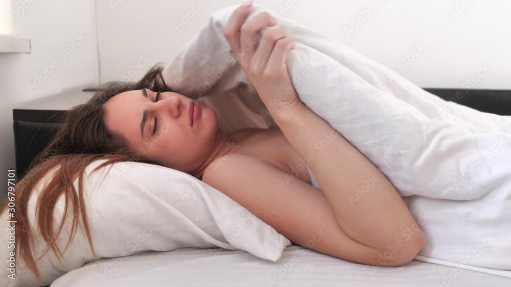 Sleepy brunette woman waking up in bed in the morning and does not want to get out of bed. not a good morning. 4k