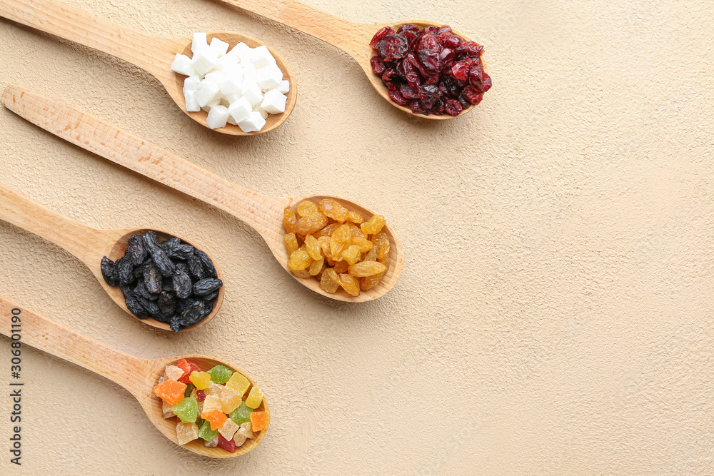 Spoons with different dried fruits on light background