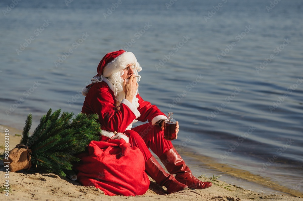Obraz premium Authentic Santa Claus with bottle of drink relaxing on beach