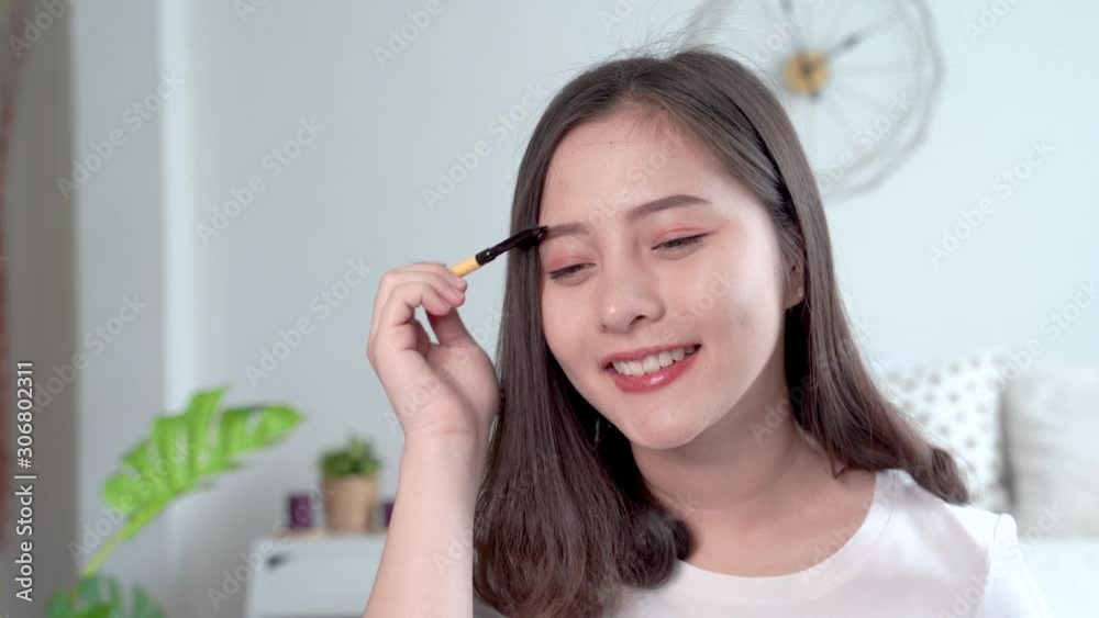 Beautiful Asian women makeup themselves by using a brush to apply eyebrows Beautiful Asian women makeup themselves by using a brush to apply eyebrows