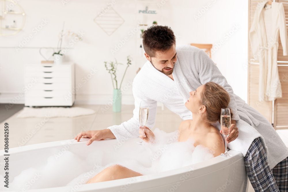 Happy young couple drinking champagne in bathroom