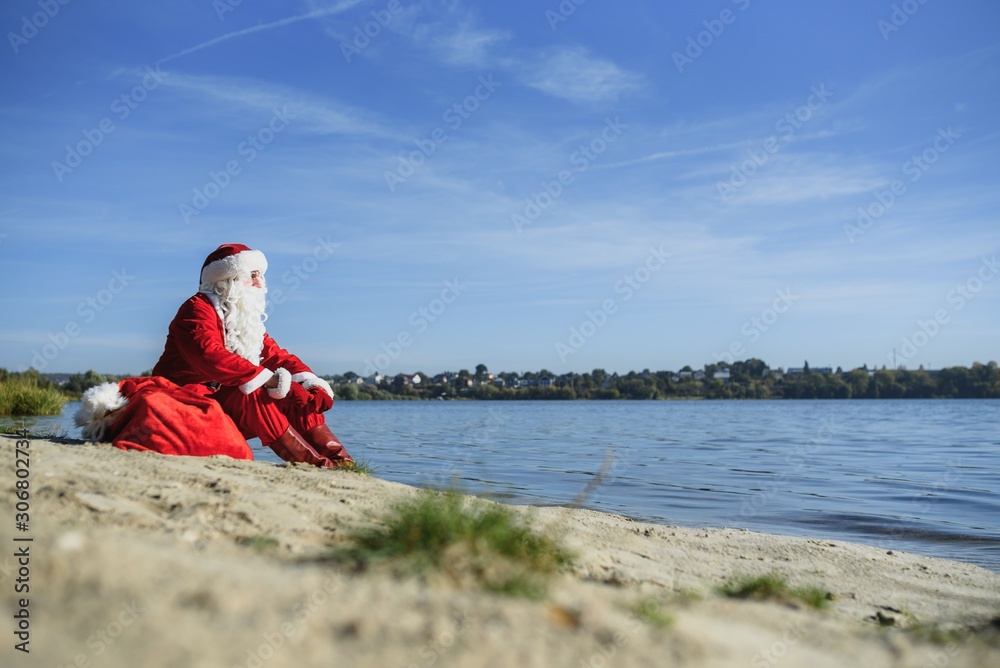 Santa Claus with at big Christmas sack full of gifts stay at ocean tropical sandy beach - X-mas or New Year's travel vacation discounts and travel agencies price reductions concept