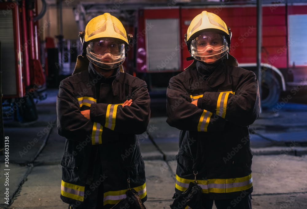 Portrait of two young firemen in uniform standing inside the fire station . Portrait of two young firemen in uniform standing inside the fire station .