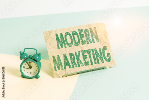 Text sign showing Modern Marketing. Business photo text methodology that connects brands with real customer Mini size alarm clock beside a Paper sheet placed tilted on pastel backdrop