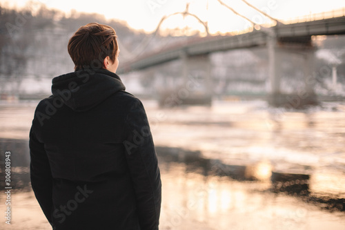 Back view of thoughtful young man looking at river while standing outdoors in winter