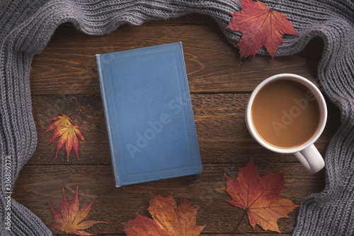 Autumn, cozy composition. Warm scarf, book, cup of coffee, maple leaves, on wooden background. Flat lay, top view, copy space.