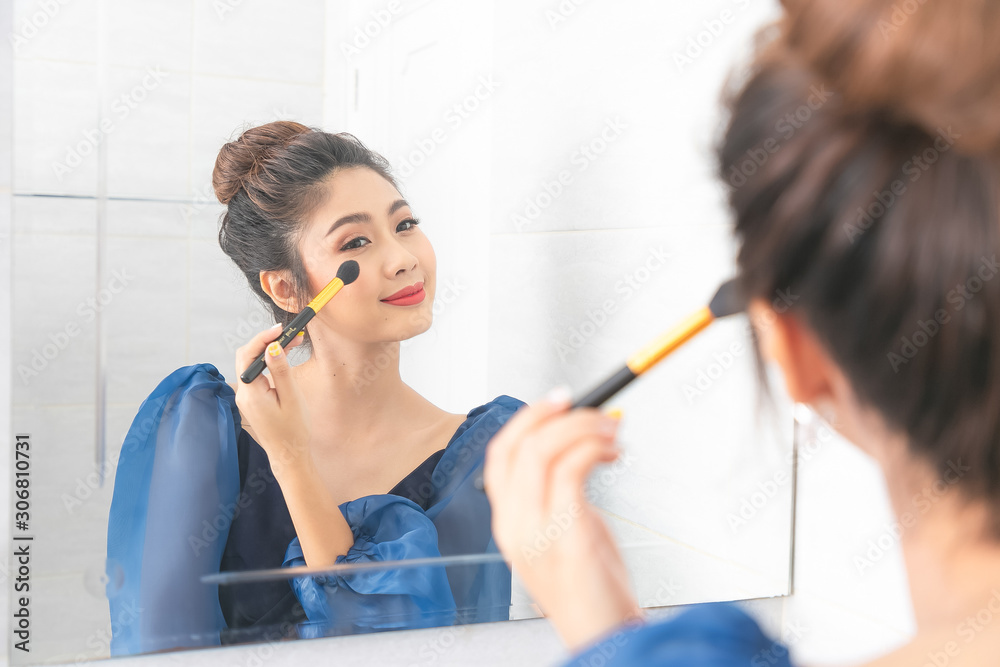 Young asian woman with makeup brush and highlighting palette looking to mirror at bathroom. Young asian woman with makeup brush and highlighting palette looking to mirror at bathroom.