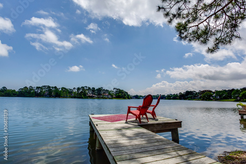 Two red chairs at the end of the dock on the river