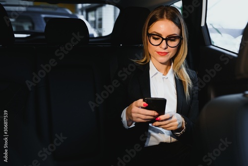 Some sort of interesting information. Smart businesswoman sits at backseat of the luxury car with black interior. © Serhii