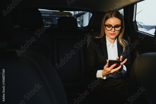 Some sort of interesting information. Smart businesswoman sits at backseat of the luxury car with black interior.
