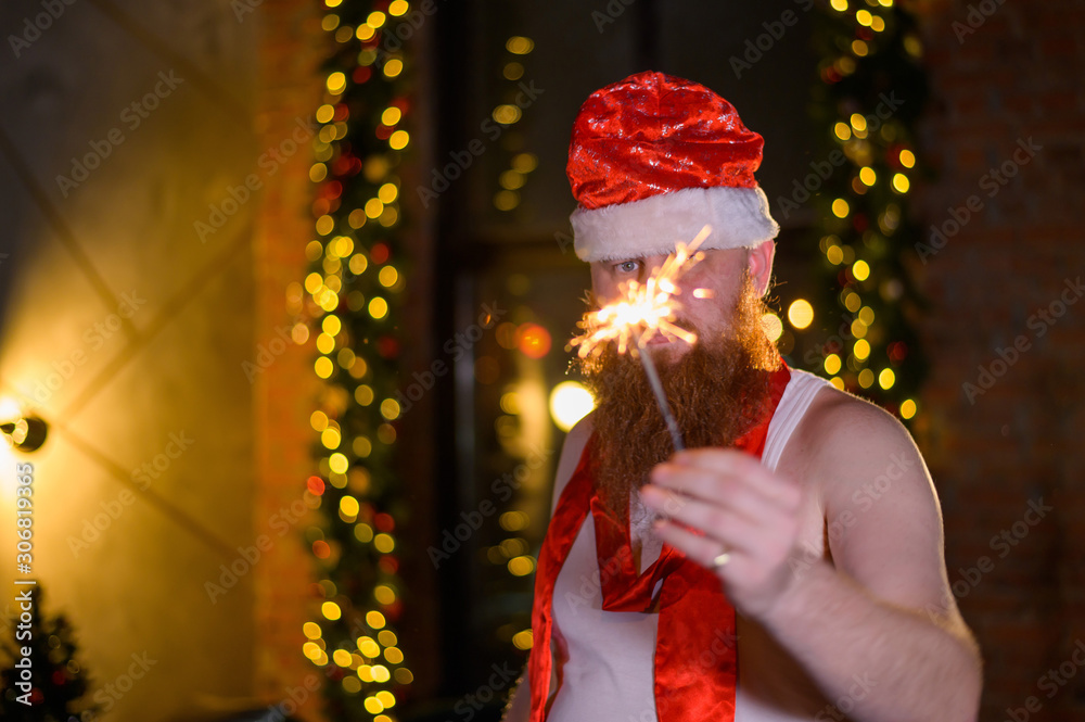 Santa with christmas sparkles. A man with a red beard in a Santa Claus hat jokingly makes a glamorous photo.