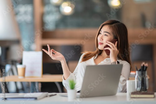 young businesswoman speaking on the phone with her customer in comfortable workplace