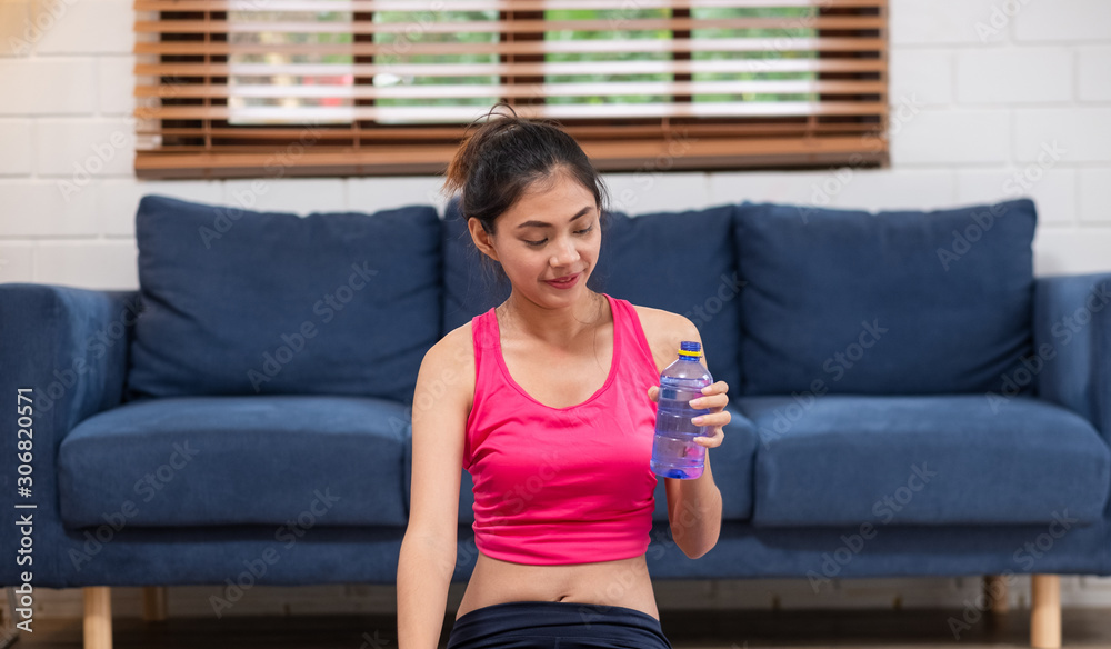  Young asian woman take a rest after training and drinking water  after workout in living room