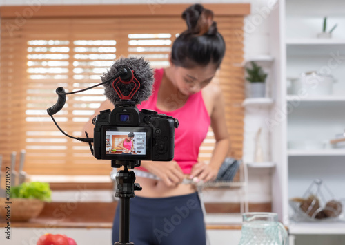 Young Asian blogge holding measuring tape around her wais while recording video on camera at home.media influencer reviewing and marketing concept
