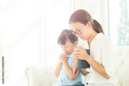 Religious Christian girl praying with her mother indoors