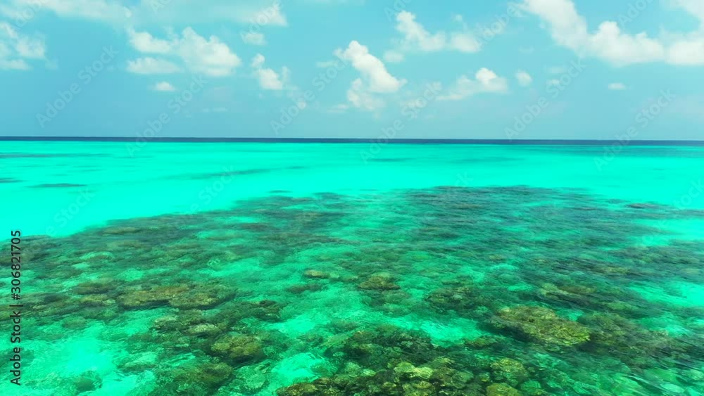 Bright turquoise lagoon with beautiful rocks and coral reef on sea bottom under bright morning sky with white clouds, copy space