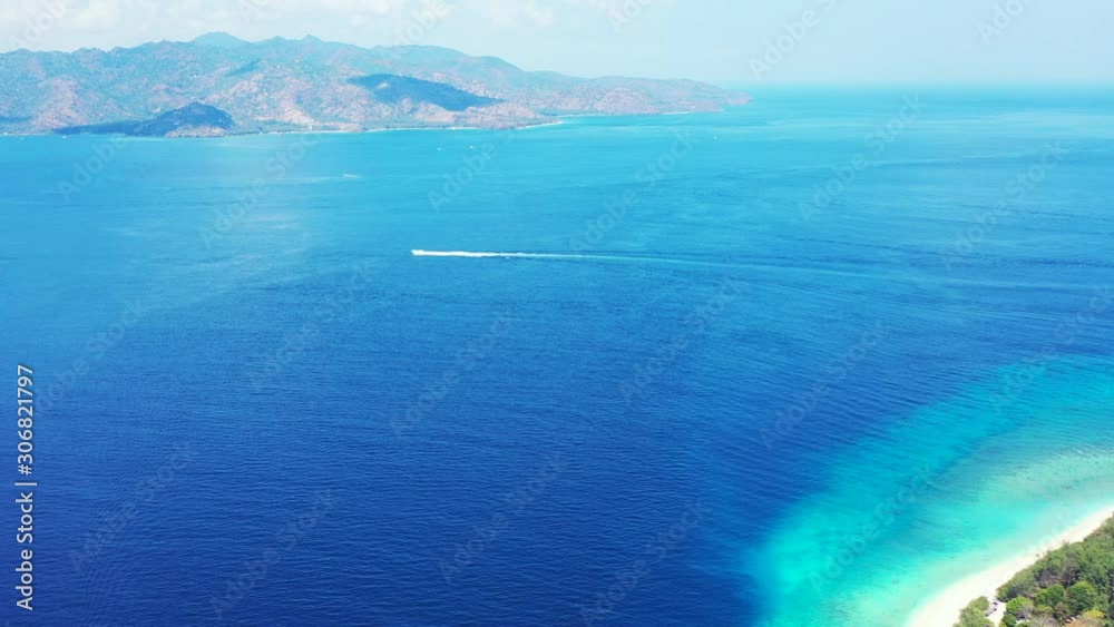 Boat sailing across blue sea stream between two shores of tropical islands with white exotic beaches on morning of Balinese coastline Boat sailing across blue sea stream between two shores of tropical islands with white exotic beaches on morning of Balinese coastline