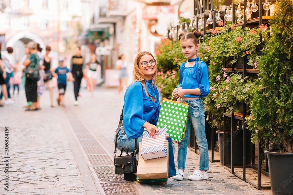 Young mother and her daughter doing shopping together. woman with girl child after shopping in street. woman with daughter with shopping bags outdoors. Woman and her daughter after shopping