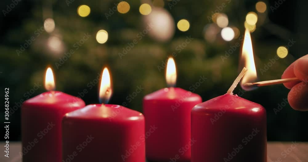 light the fourth red candle of an advent wreath in front of a christmas tree