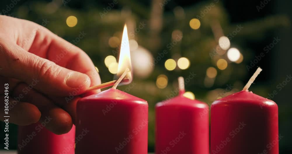light the first red candle of an advent wreath in front of a christmas tree