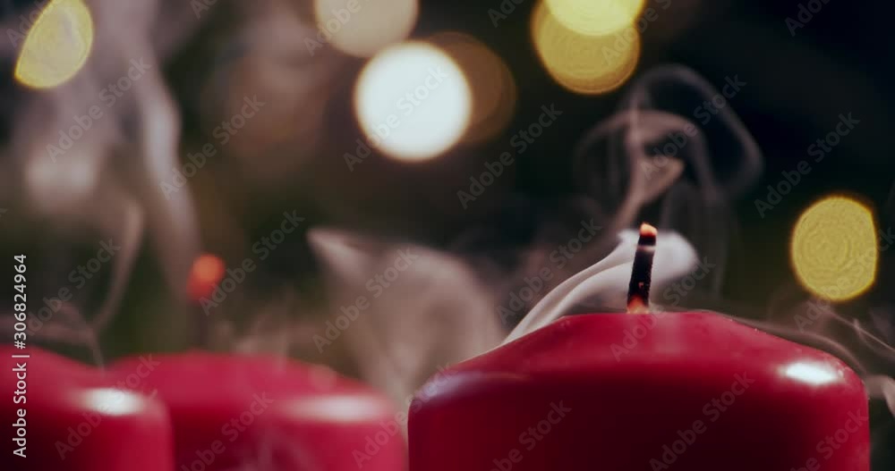 blowing out two red candles in front of a christmas tree