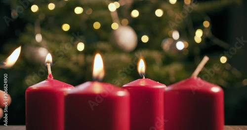 light the third red candle of an advent wreath in front of a christmas tree photo