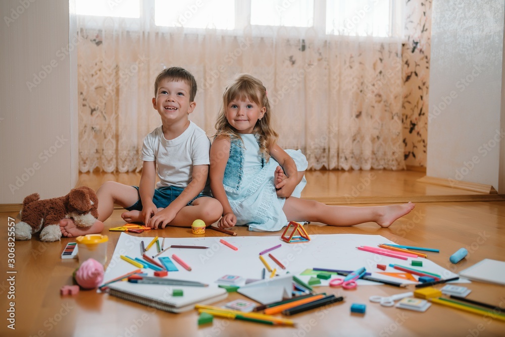 Kids drawing on floor on paper. Preschool boy and girl play on floor with educational toys - blocks, train, railroad, plane. Toys for preschool and kindergarten. Children at home or daycare.