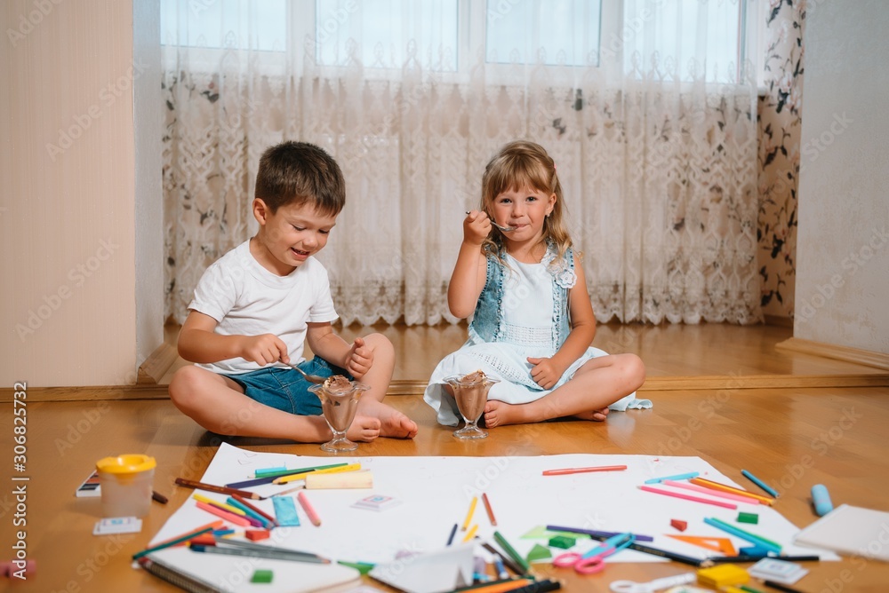 Obraz premium Kids drawing on floor on paper. Preschool boy and girl play on floor with educational toys - blocks, train, railroad, plane. Toys for preschool and kindergarten. Children at home or daycare.