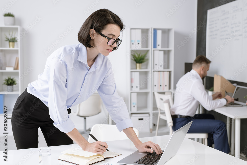 Confident businesswoman bending over desk in front of laptop while networking Confident businesswoman bending over desk in front of laptop while networking