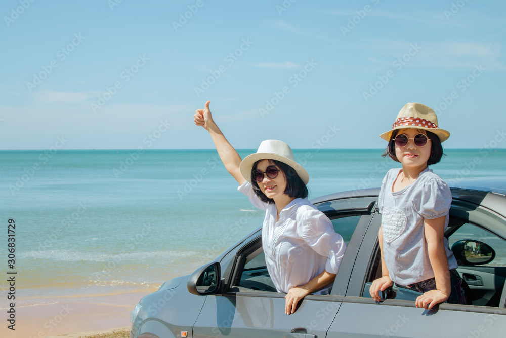 Summer Vacation and Car Trip Concept : Family car trip at the sea, Woman and child cheerful raising their hands up and feeling happiness in silver car with seascape in the background.